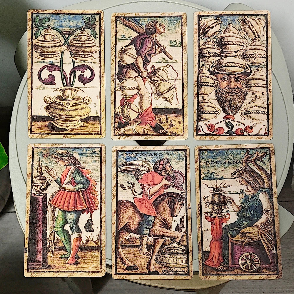 Sola Busca Tarot — six face-up Minor Arcana: 3 of Cups (three ornate classical urns with scrollwork), 3 of Wands (armoured figure carrying bundles of wands on horseback), 10 of Coins (bearded grotesque face beneath tower of coin-discs with pomegranate border), Page of Wands (jester figure with lantern beside a column), Matanabo (Knight of Coins, armoured rider on horseback), Polisena (Queen of Coins, seated woman with an urn at a spinning wheel)