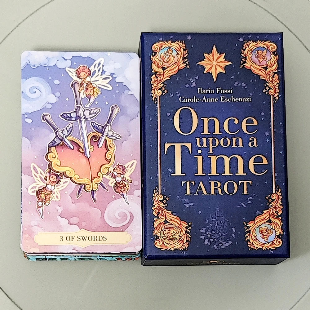 Once Upon a Time Tarot — 3 of Swords card (fairies holding three silver swords piercing a gold heart amid clouds and stars) beside the deep navy rigid box with gilt baroque border, compass star, and authors Ilaria Fossi and Carole-Anne Eschenazi in gold lettering