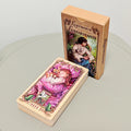 Lustrous Lenormand full deck face-down showing crimson and gold embossed cross-and-wreath card backs beside illustrated peach tuck box showing cards 1 Rider, 2 Clover, 3 Ship, 4 House on front panel