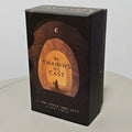 The Shadows We Cast Tarot — rigid box front featuring robed figure silhouette beneath a crescent moon in an arched forest portal