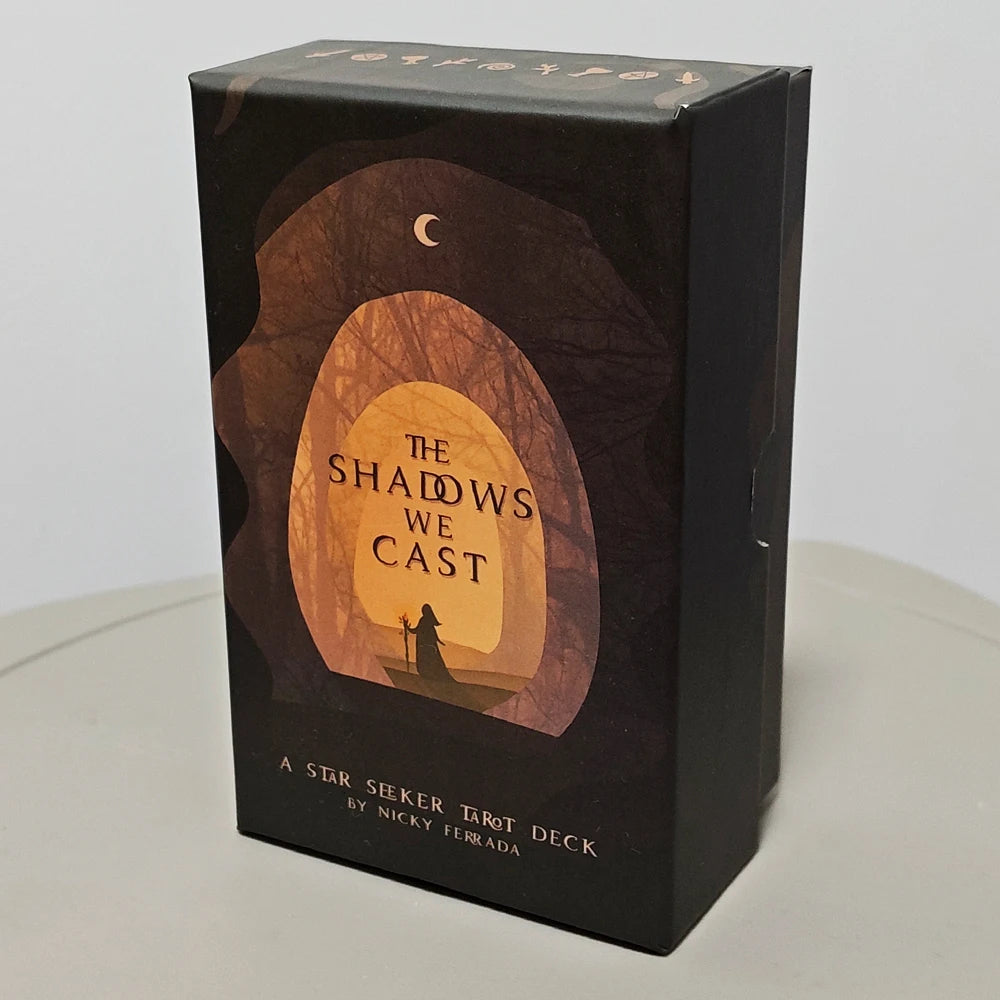 The Shadows We Cast Tarot — rigid box front featuring robed figure silhouette beneath a crescent moon in an arched forest portal