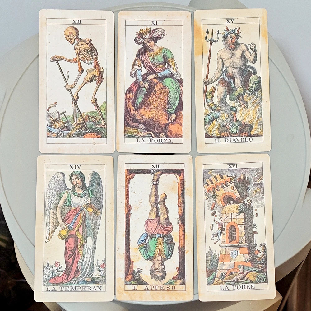 Tarocco Soprafino 1830 — six Major Arcana face-up on round white table: XIII Death (striding skeleton with scythe amid ruins), XI La Forza (crowned figure seated on lion), XV Il Diavolo (Neptune-like devil with trident standing over flames), XIV La Temperan. (winged angel pouring between vessels), XII L’Appeso (man hanging upside down from wooden frame), XVI La Torre (crumbling tower struck by lightning with figures falling)