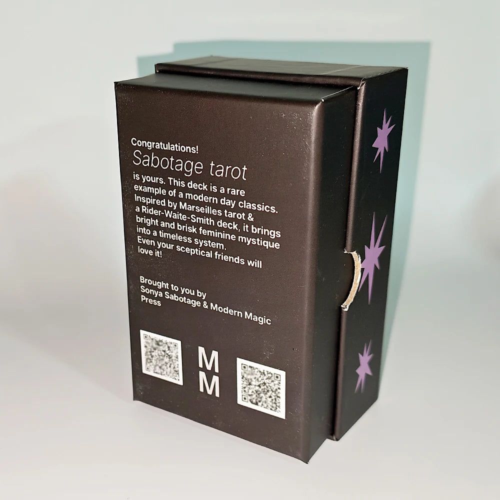 Sabotage Tarot matte black rigid box rear showing publisher text: ‘Sabotage Tarot is yours. This deck is a rare example of a modern day classic. Inspired by Marseilles tarot and a Rider-Waite-Smith deck, it brings a bright and brisk feminine mystique into a timeless system.’ Brought to you by Sonya Sabotage & Modern Magic Press. Pink star motifs on sides.