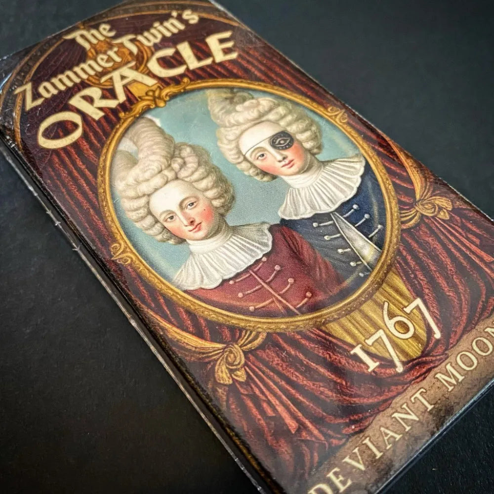 The Zammer Twin’s Oracle crimson tuck box close-up: gilt oval portrait of the two Zammer Twins in powdered wigs — one masked with an eye, one serene — on rich red velvet draping background; dated 1767, Deviant Moon Inc.