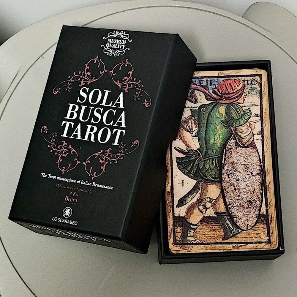Sola Busca Tarot matte black rigid box open showing full card deck face-up with a named figure card on top; box lid reads: Sola Busca Tarot, The Tarot masterpiece of Italian Renaissance, Official licensed product by Pinacoteca di Brera, Lo Scarabeo beetle seal, Museum Quality