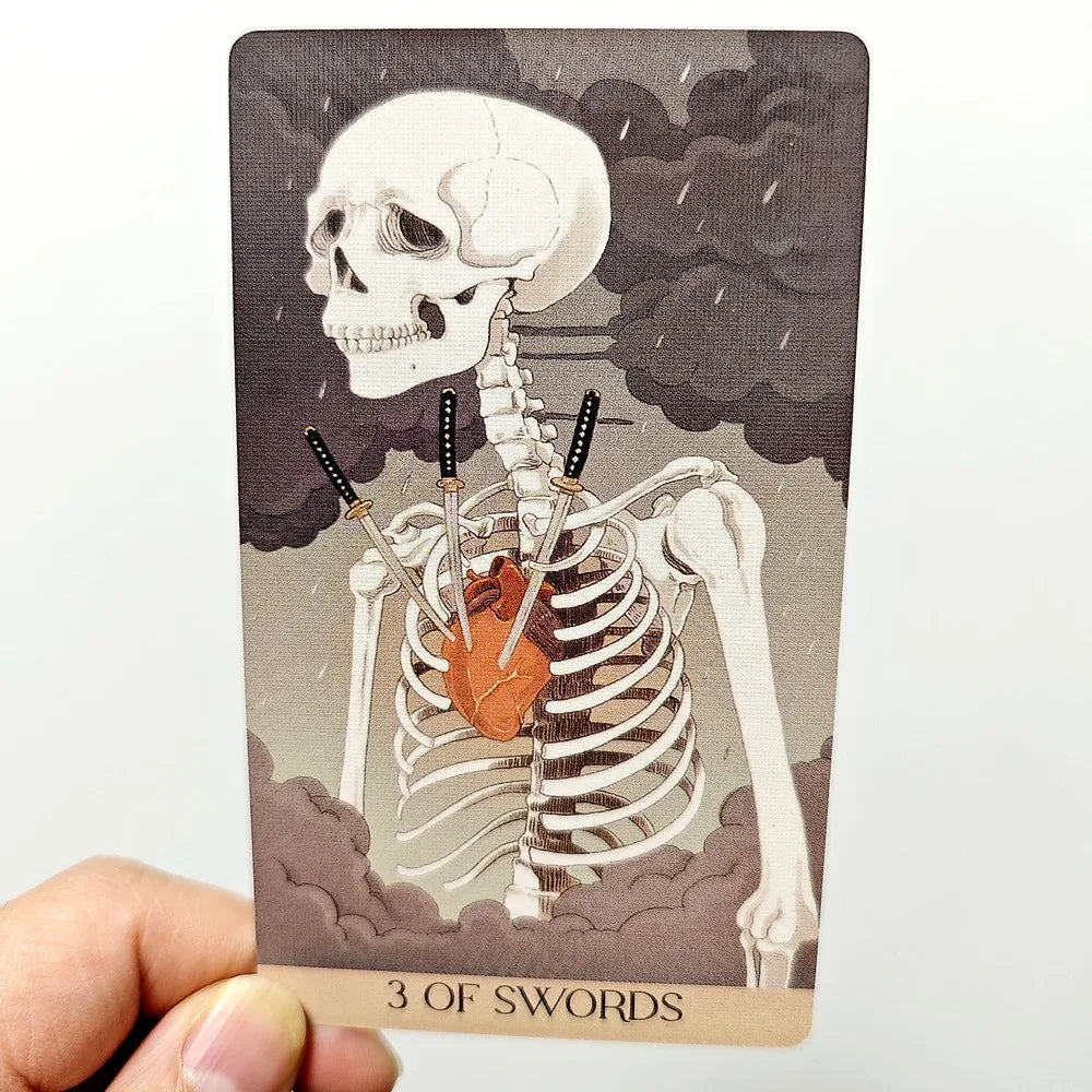 Yōkai Tarot — Three of Swords card held up showing skeleton with katana swords through ribcage, storm background