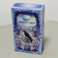 Silent Desolate Tarot blue art nouveau box featuring a raven perched among white peonies beneath the dripping title plaque ‘Silent Desolate Tarot’ on a cerulean wave-patterned background