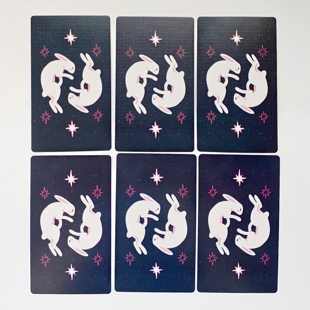 Sabotage Tarot — six dark navy card backs showing dancing white rabbit pairs amid pink and purple eight-pointed star motifs on a dark ground; reversible design