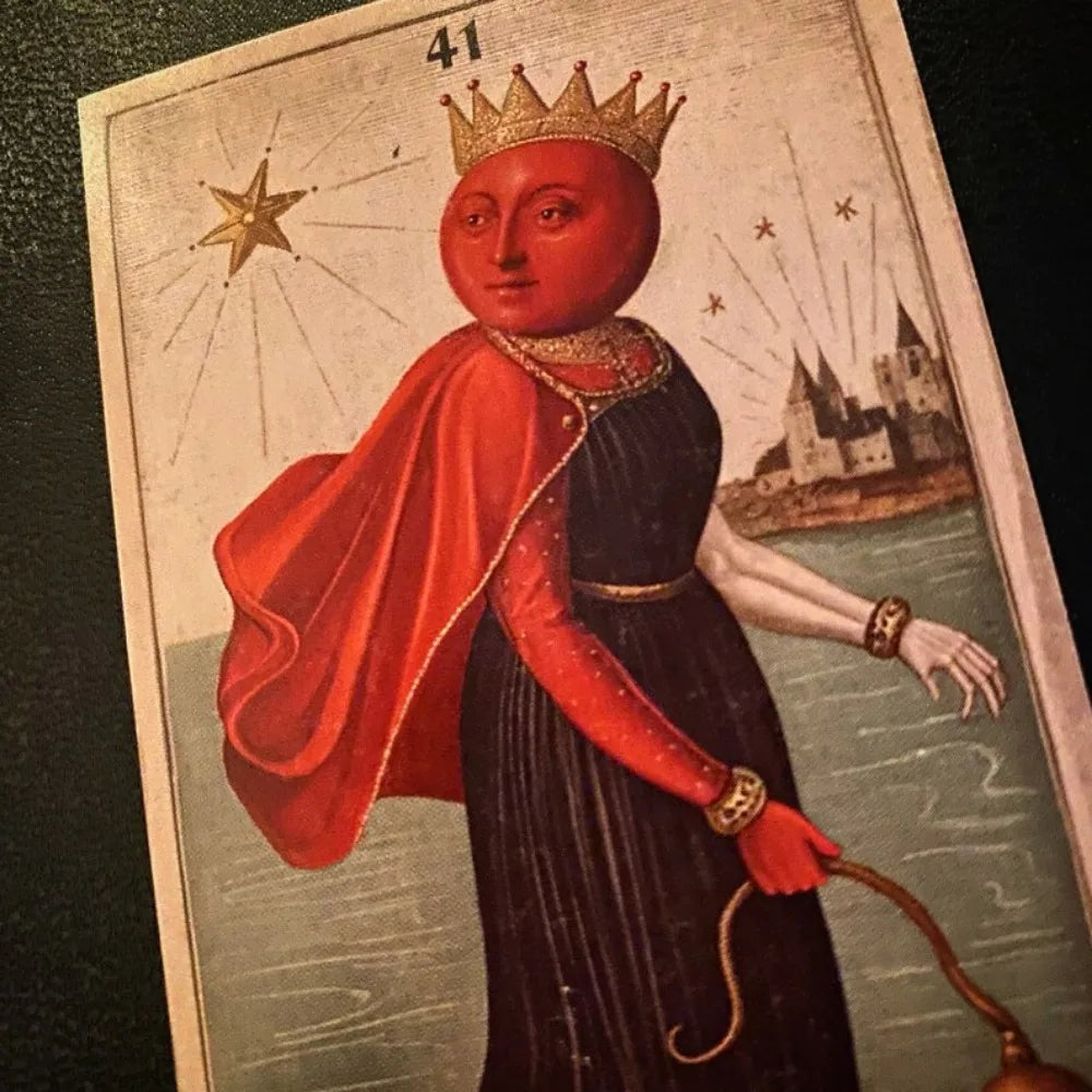 The Zammer Twin’s Oracle card 41: crowned figure with a red spherical head in black gown and red cape, holding a leash, castle in background on pale blue sky; gold star to left