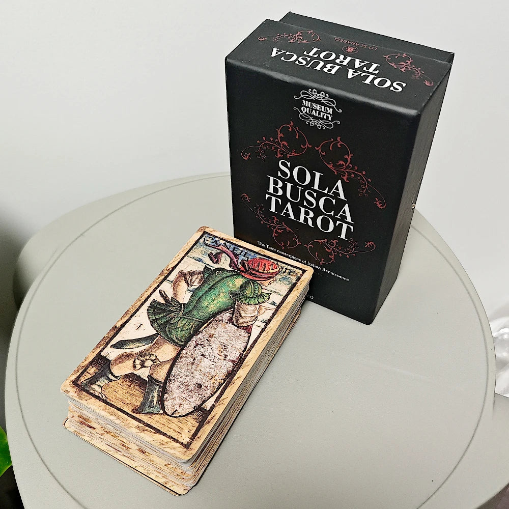 Sola Busca Tarot full deck face-up beside the matte black Lo Scarabeo rigid box on a round white table; top card shows an armoured Renaissance soldier figure