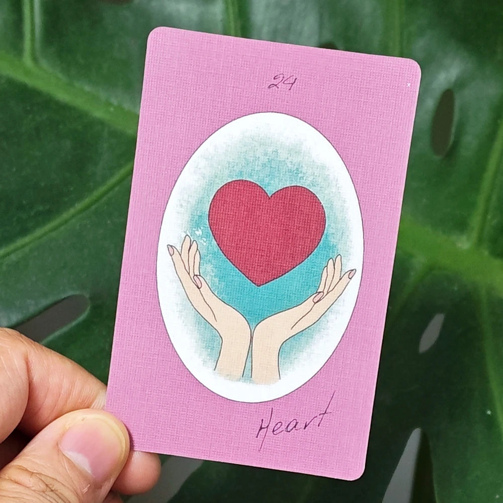 Ribbon Lenormand card 24 — Heart: two open hands cradling a large red heart on a teal background, pink card with handwritten label