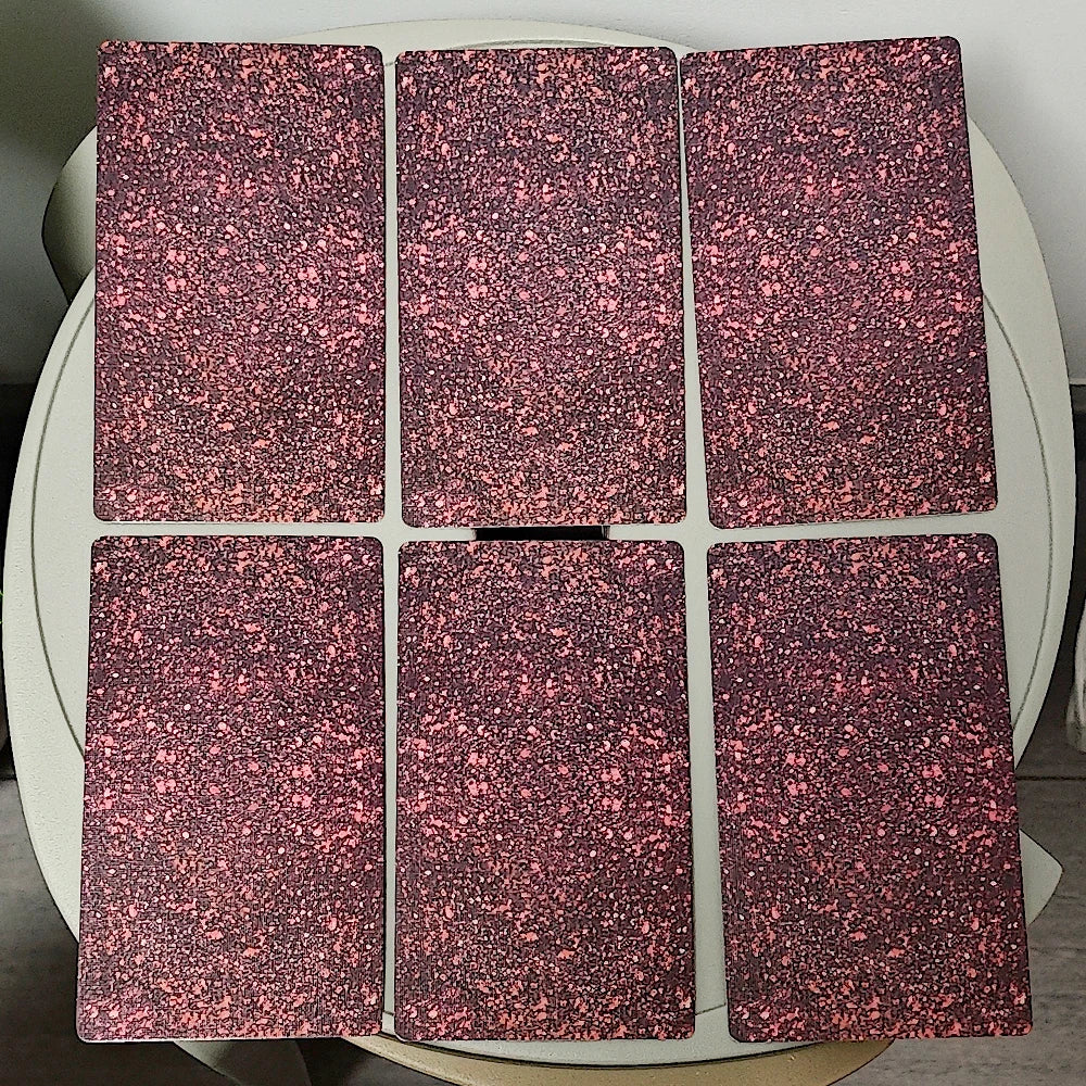 Sola Busca Tarot — six rose-pink holographic glitter card backs arranged on a round white table; the iridescent pink-and-burgundy glitter pattern catches the light
