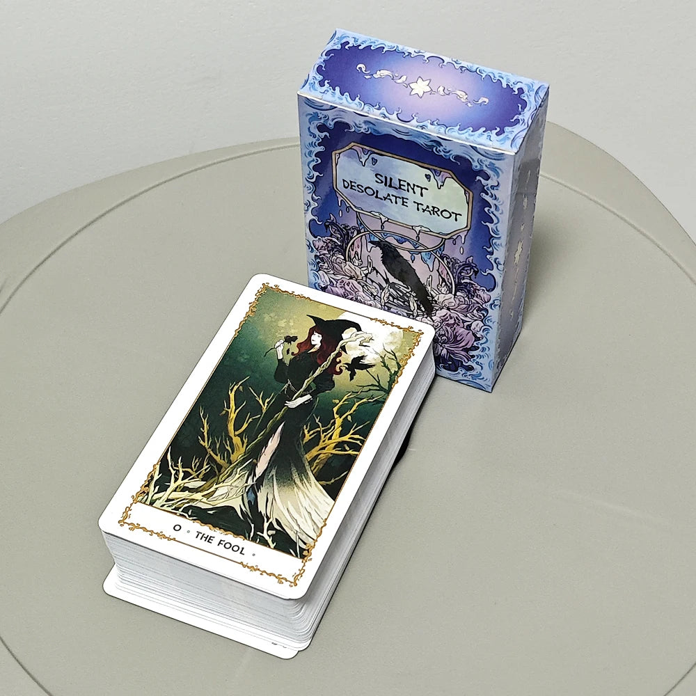 Silent Desolate Tarot — full 78-card deck face-up with The Fool on top (witch in black dress among bare branches with a raven) beside the blue art nouveau box