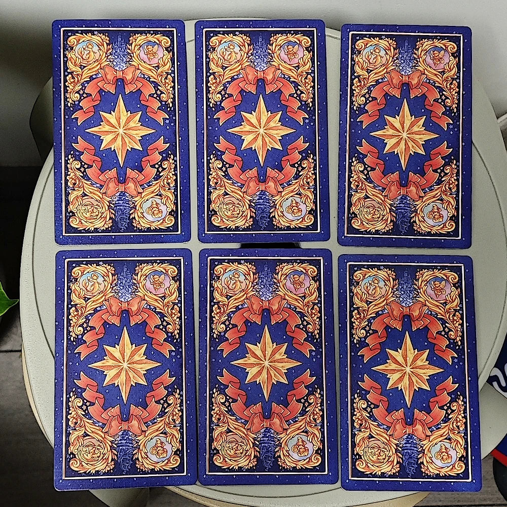 Once Upon a Time Tarot — six deep navy card backs showing gold eight-pointed compass star framed by crimson ribbons and gilt baroque scrollwork, with fairy vignettes in top and bottom medallions; fully reversible design
