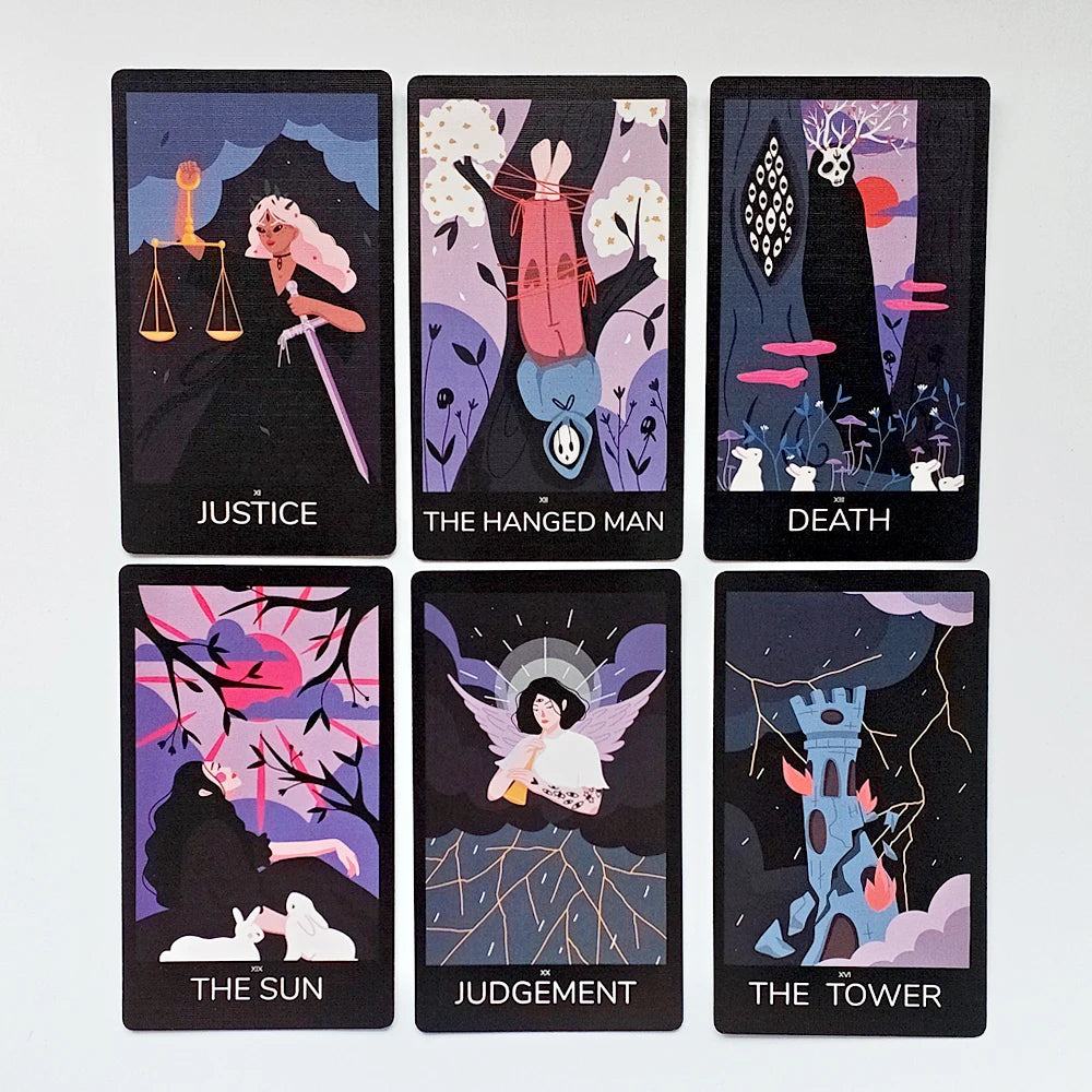 Sabotage Tarot — six Major Arcana face-up: XI Justice (white-haired figure with scales and sword), XII The Hanged Man (pink-clad figure suspended upside-down from tree), XIII Death (antlered skull over dark mushroom woodland with white rabbits), XIX The Sun (figures beneath bare branches with rabbit at dusk), XX Judgement (winged angel with halo descending), XVI The Tower (blue tower struck by lightning with flames)